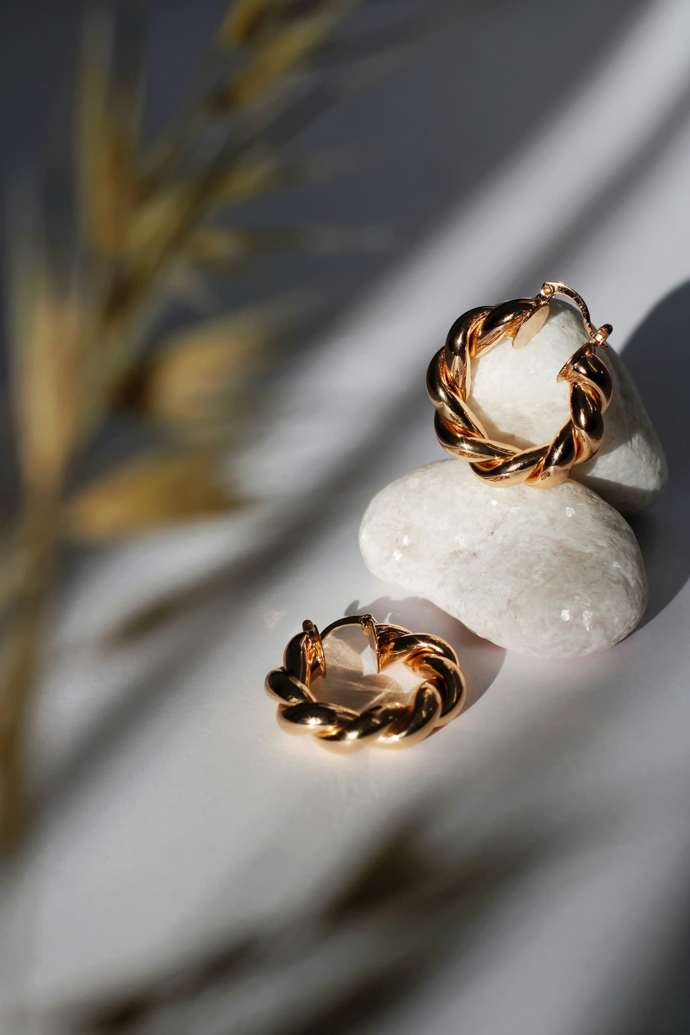 Twisted gold-tone hoop earrings resting on pale stones in soft sunlight